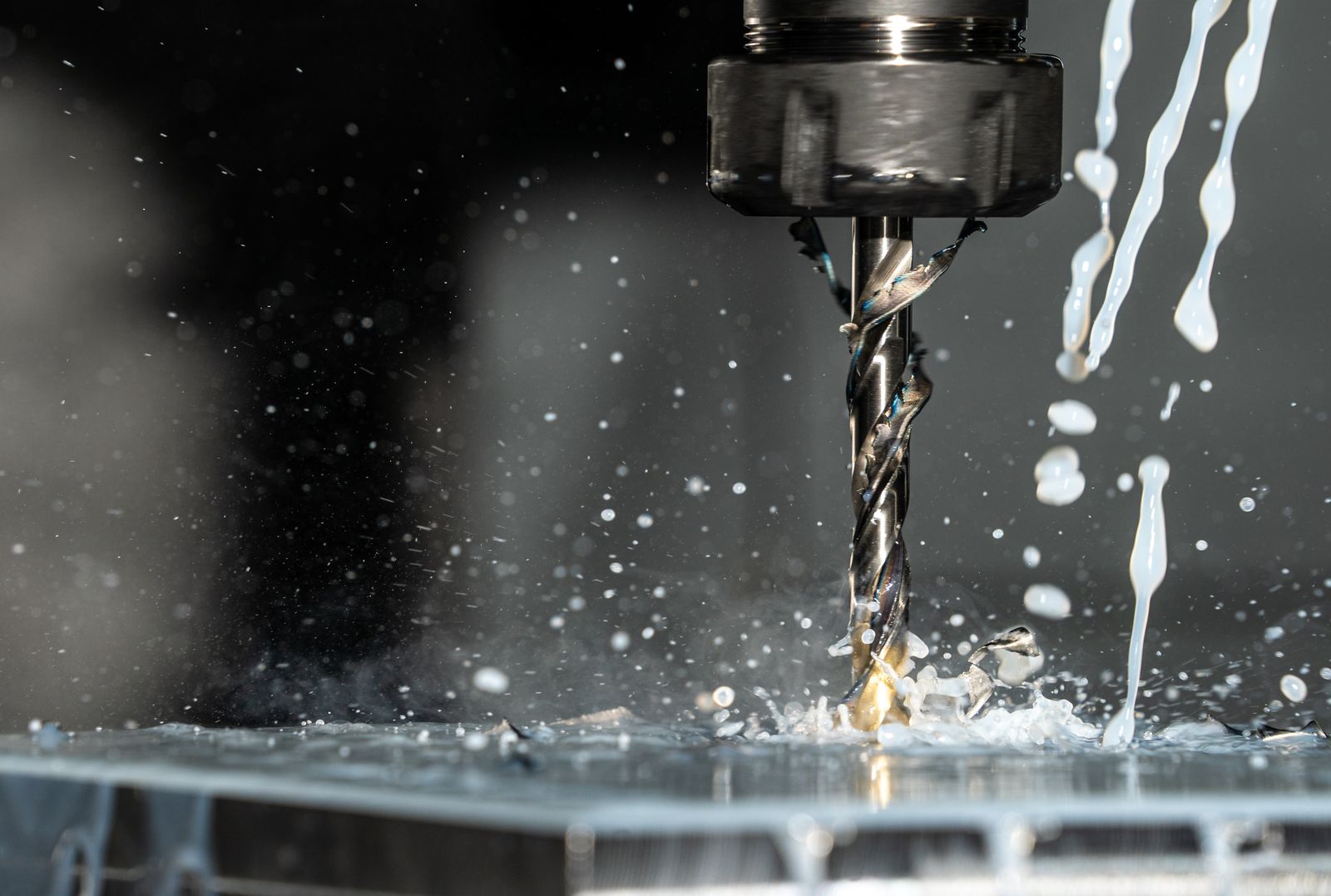 A CNC drill bit machining metal with cutting fluid