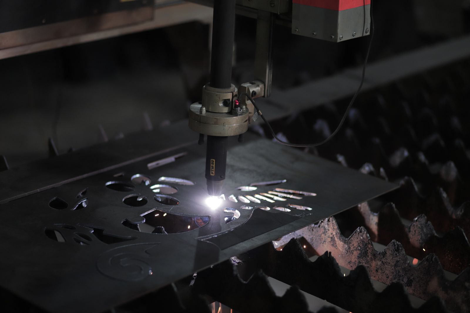 A CNC cutting head slicing a shaped part from a steel plate