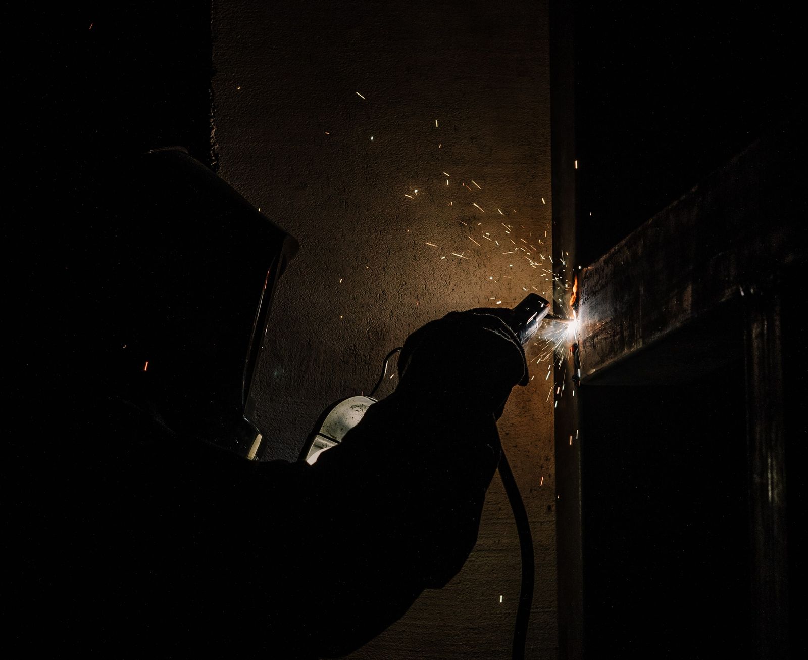A welder joining structural steel with sparks flying in a darkened shop